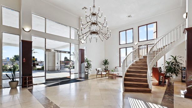 A spacious lobby with a chandelier, a staircase, and large windows. - Brookhurst Plaza Inn (Anaheim)