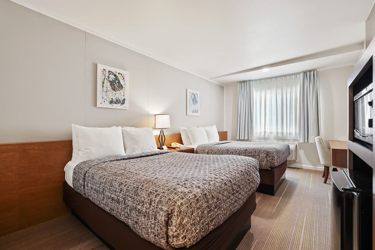 Habitación de hotel con dos camas, un escritorio, televisión y obras de arte en las paredes.