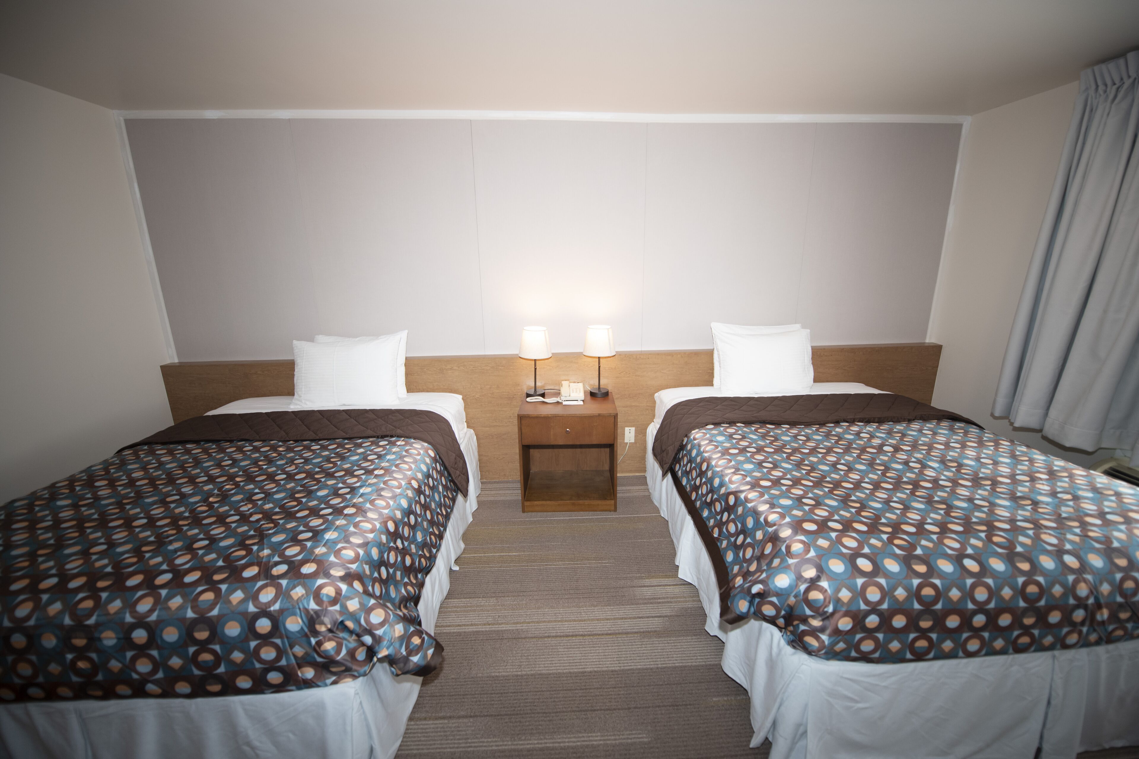 Une chambre d’hôtel avec deux lits, une table de chevet avec des lampes et un mur sobre.