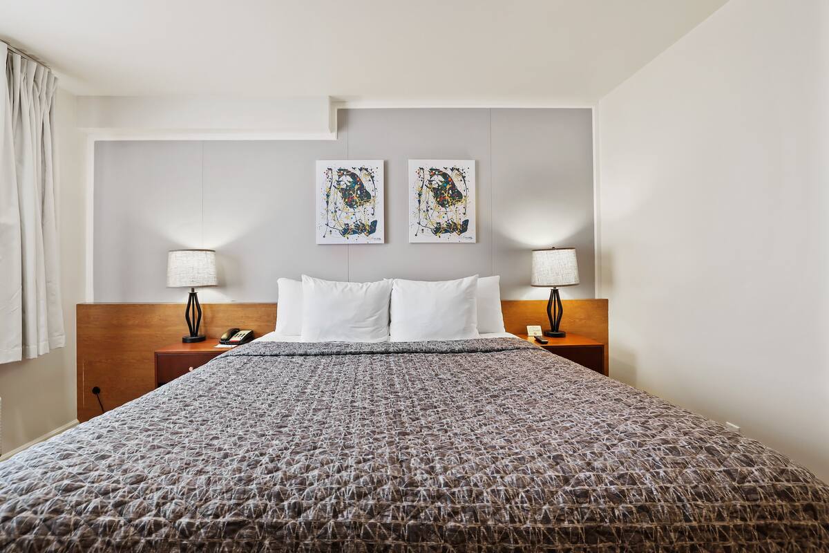 Habitación de hotel con una cama grande, dos lámparas de noche, un cabecero de madera y dos cuadros abstractos en la pared.