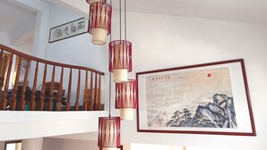 Un escalier avec des rampes en bois et une lampe suspendue, rouge et beige. Un tableau encadré est accroché au mur.