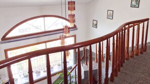 Un escalier avec des balustrades en bois et une main courante, menant à un palier d’où l’on peut admirer un jardin à travers une grande fenêtre en arc de cercle.