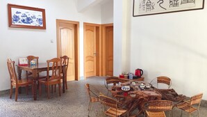 Un coin repas avec une table et des chaises en bois, une table basse en osier et un tableau traditionnel chinois accroché au mur.
