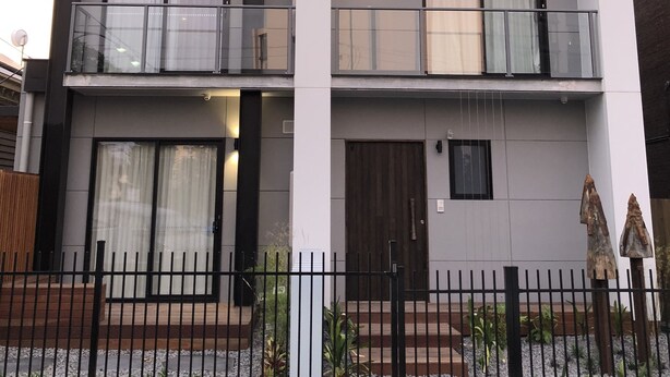 Um edifício moderno de dois andares com varanda, janelas amplas e entrada com portão.