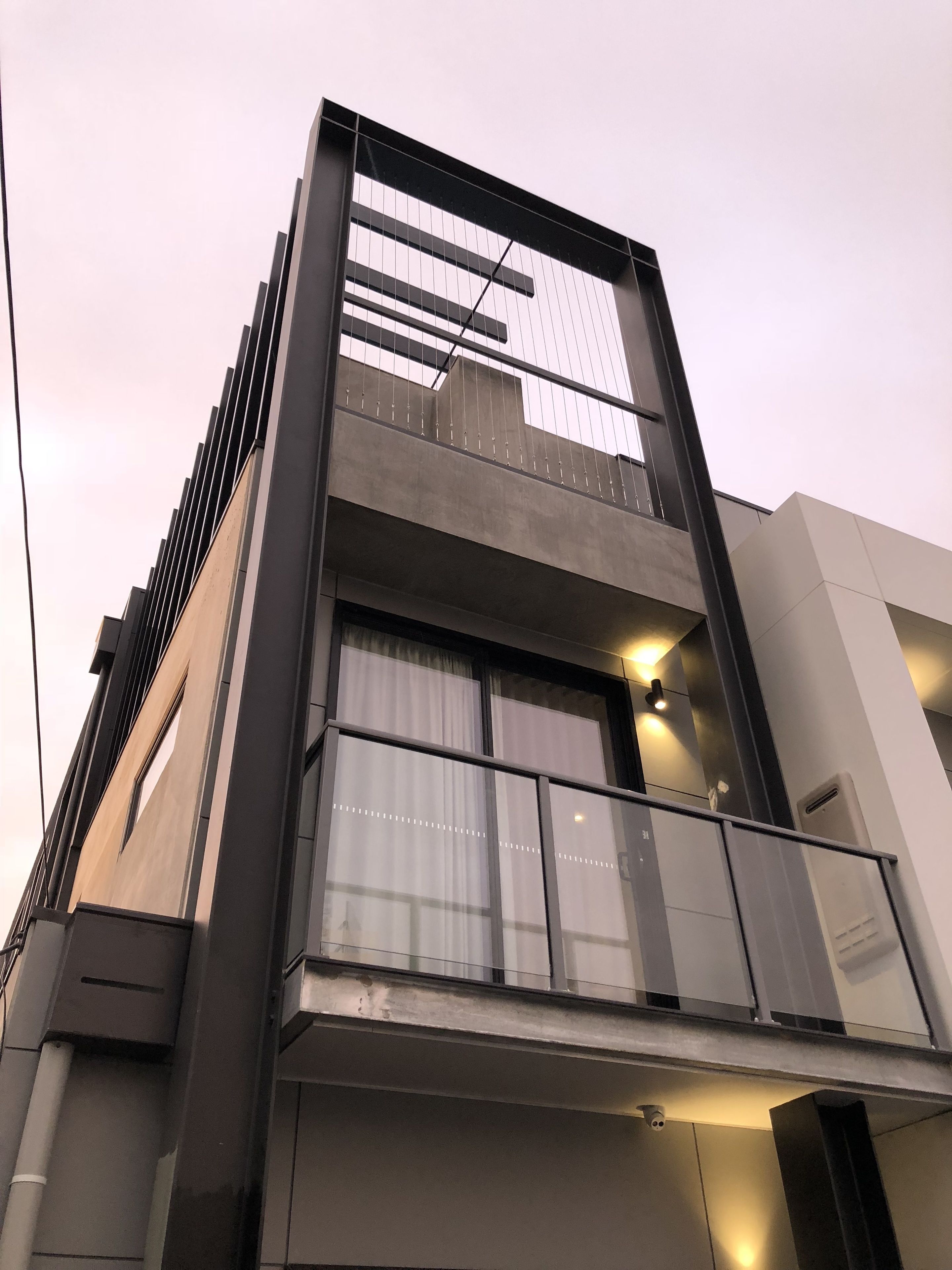 Un edificio moderno con balcón, ventanas amplias y una unidad de aire acondicionado visible.