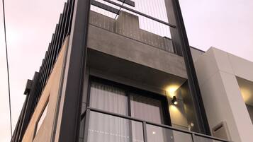 Un edificio moderno con balcón, ventanas amplias y una unidad de aire acondicionado visible.