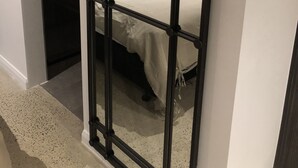Quarto com cama, cabeceira de madeira, luminária pendente e divisória de metal preto.