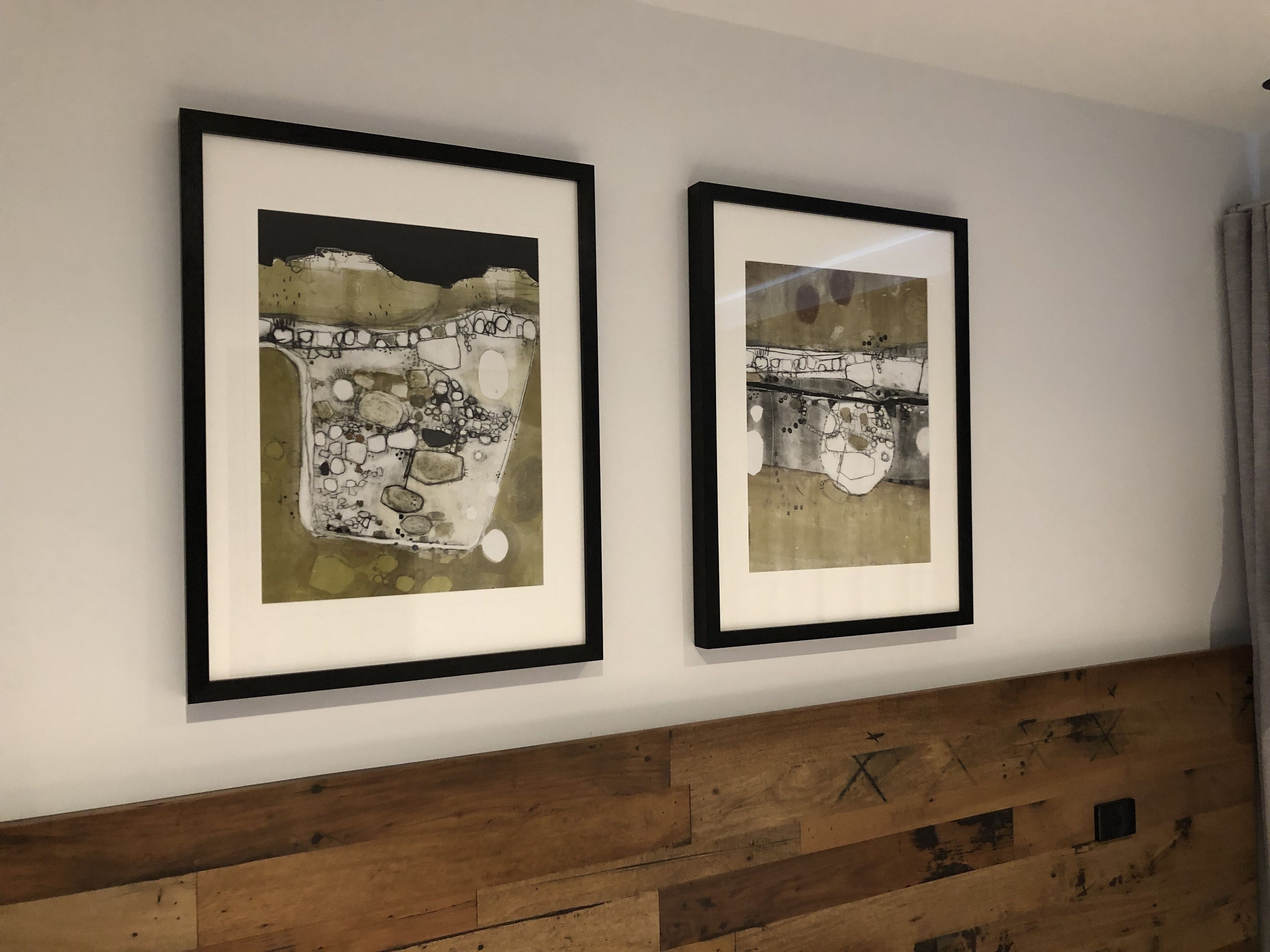 Two framed artworks on a wall with a wooden headboard below.
