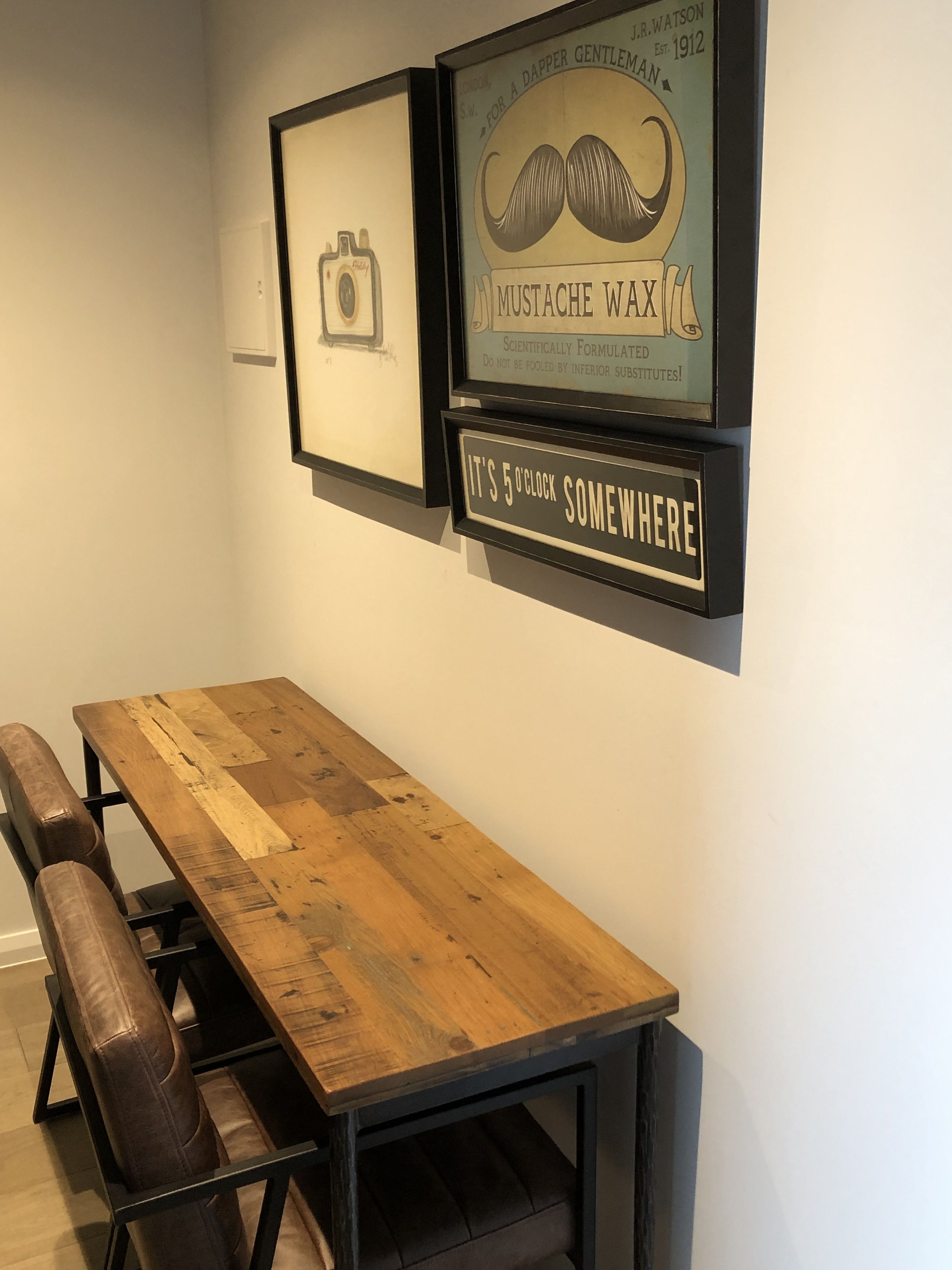 A wooden dining table with benches, framed pictures on the wall, and a sign that reads "It's 5 o'clock somewhere."