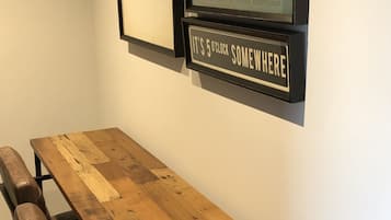 A wooden dining table with benches, framed pictures on the wall, and a sign that reads "It's 5 o'clock somewhere."