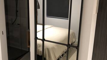 Una habitación con cama, ducha y un espejo grande.