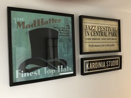 Tres letreros enmarcados: 'The Mad Hatter', 'Festival de Jazz en Central Park' y 'Kardinia Studio'.