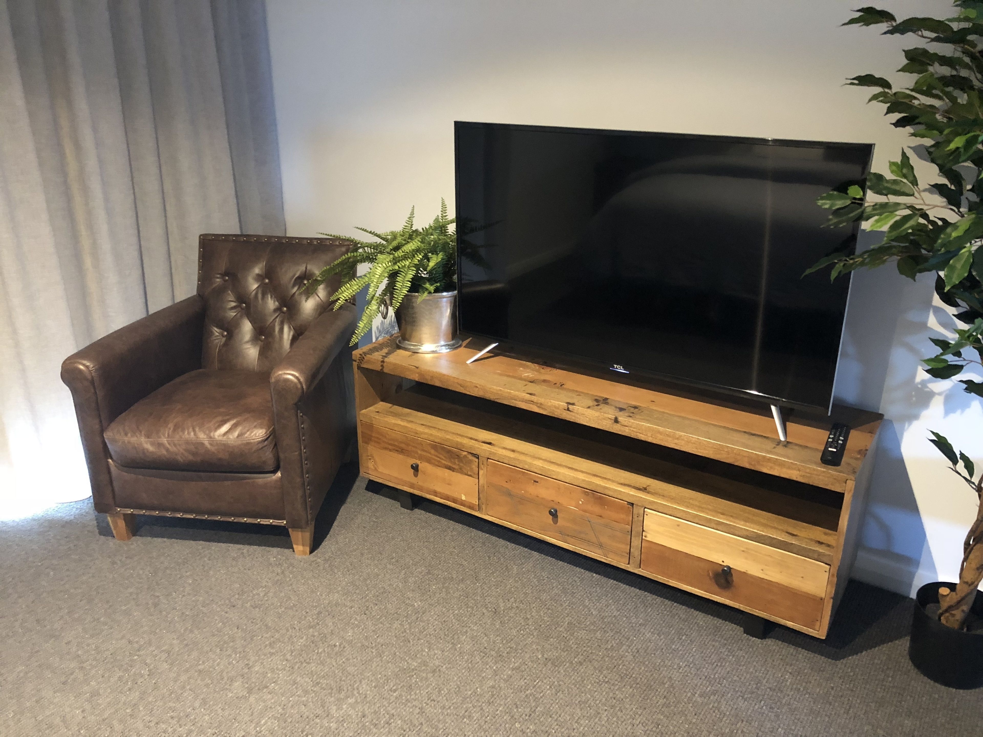 A brown leather armchair, a wooden entertainment unit with a flat-screen TV, and a potted plant.