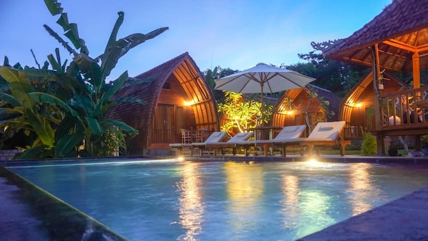A poolside area with lounge chairs and umbrellas, surrounded by wooden structures with arched roofs. - The Tandjung Cottage (Penida Island)
