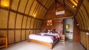 A spacious room with a large bed, wooden walls, and a small table. - The Tandjung Cottage (Penida Island)