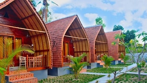 A row of wooden cabins with pitched roofs, each featuring a small porch and a staircase leading to the entrance. - The Tandjung Cottage (Penida Island)