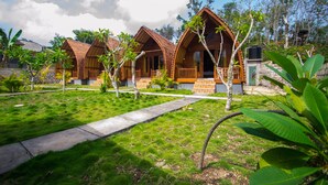 A row of wooden cabins with a grassy lawn and a concrete pathway. - The Tandjung Cottage (Penida Island)