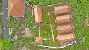 An aerial view of a traditional building with a tiled roof, surrounded by lush greenery and a paved courtyard. - The Tandjung Cottage (Penida Island)