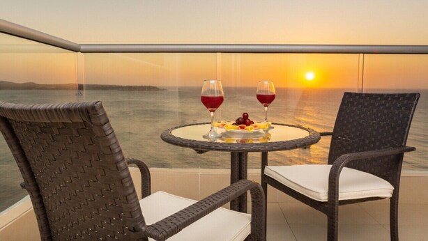A balcony with wicker chairs, a glass table, and a sunset view. - Luxury apartment facing the sea (Cartagena)
