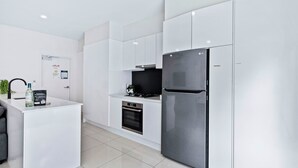 Eine moderne Küche mit weißen Schränken, einem Edelstahlkühlschrank, einem eingebauten Backofen und einer kleinen Arbeitsfläche mit Spüle und einer Flasche.
