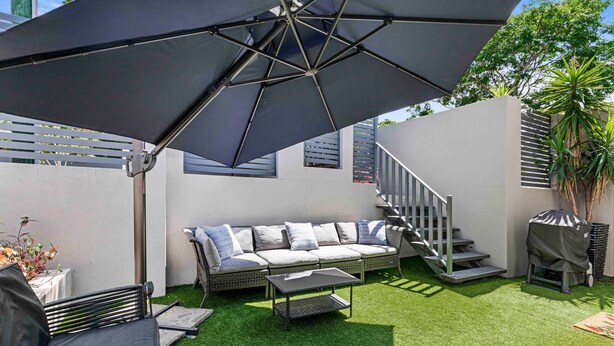 Eine Terrasse mit einer Sitzecke, einem Tisch und einem Grill.