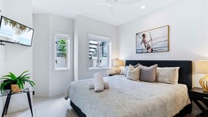 Ein modernes Schlafzimmer mit einem großen Bett, einem Deckenventilator, einem Fernseher und einem Bild an der Wand.