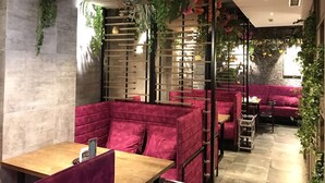 Un restaurante con asientos tapizados en rojo, plantas colgantes y una pared de piedra.
