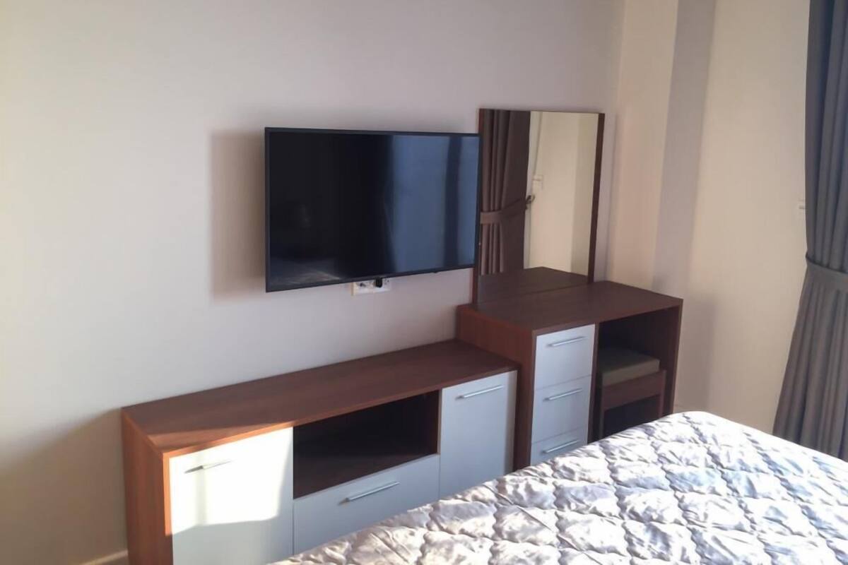 A bedroom with a bed, a TV mounted on the wall, a mirror, and a wooden dresser with drawers.