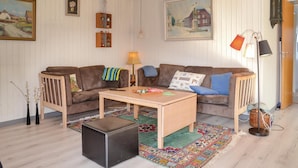 A cozy living room with a brown sofa, a wooden coffee table, and a colorful rug. There are wall-mounted shelves with decorative items and a painting of a snowy scene. - Nice home in Esbjerg V with WiFi (Esbjerg V)
