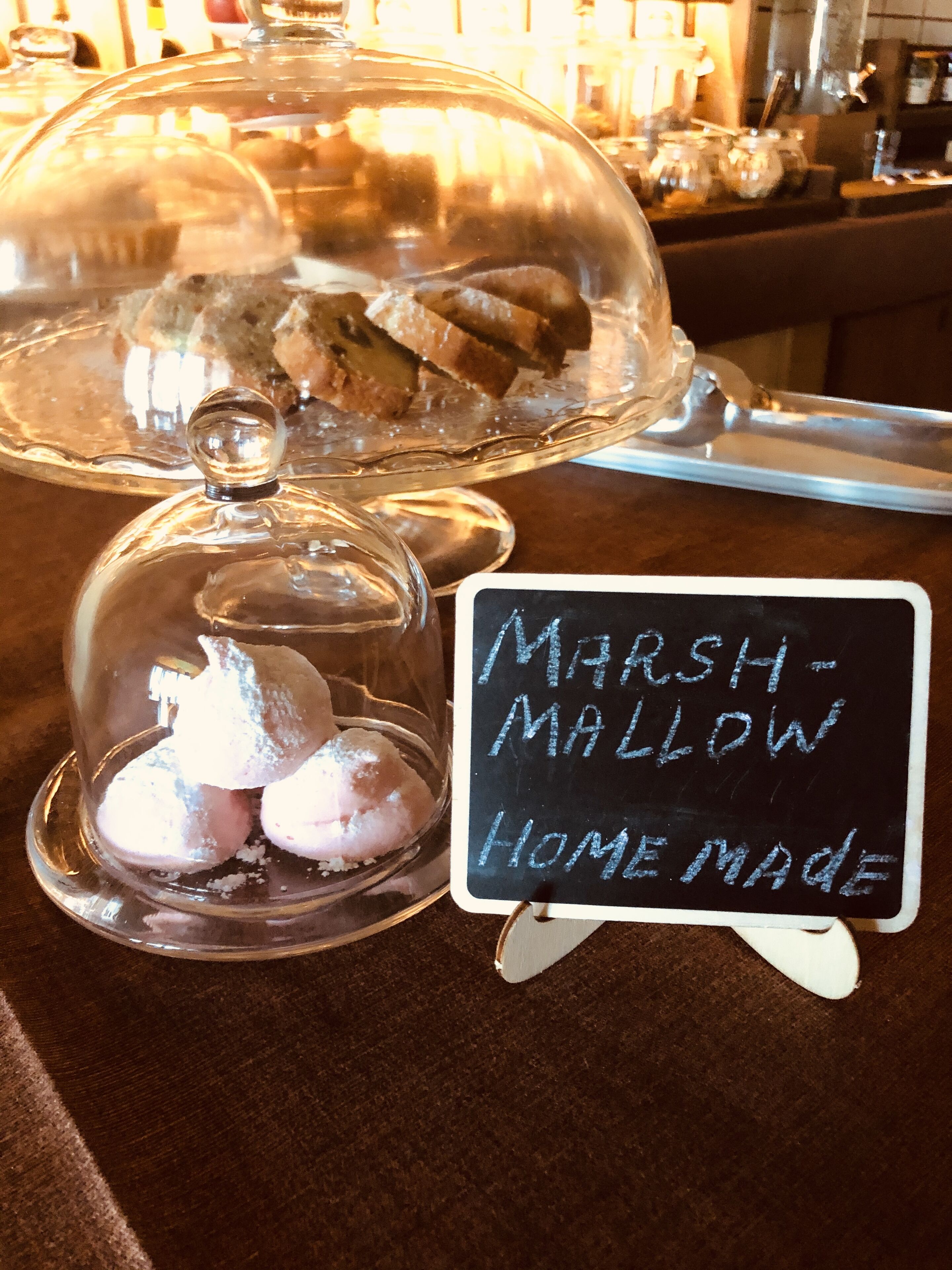 Una presentación de postres bajo una campana de cristal y un cartel que indica 'Marshmallow Hecho en Casa'.