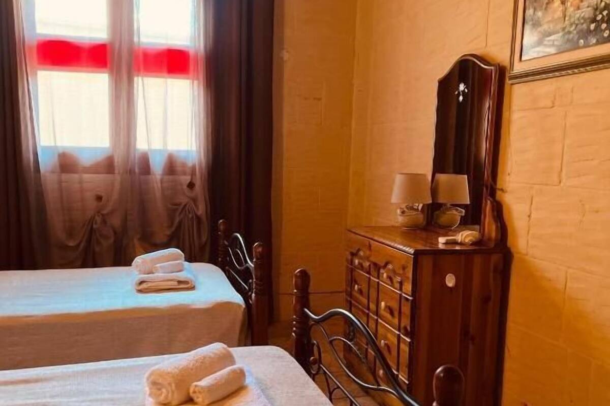 A room with two beds, a wooden dresser, a mirror, and a painting on the wall.