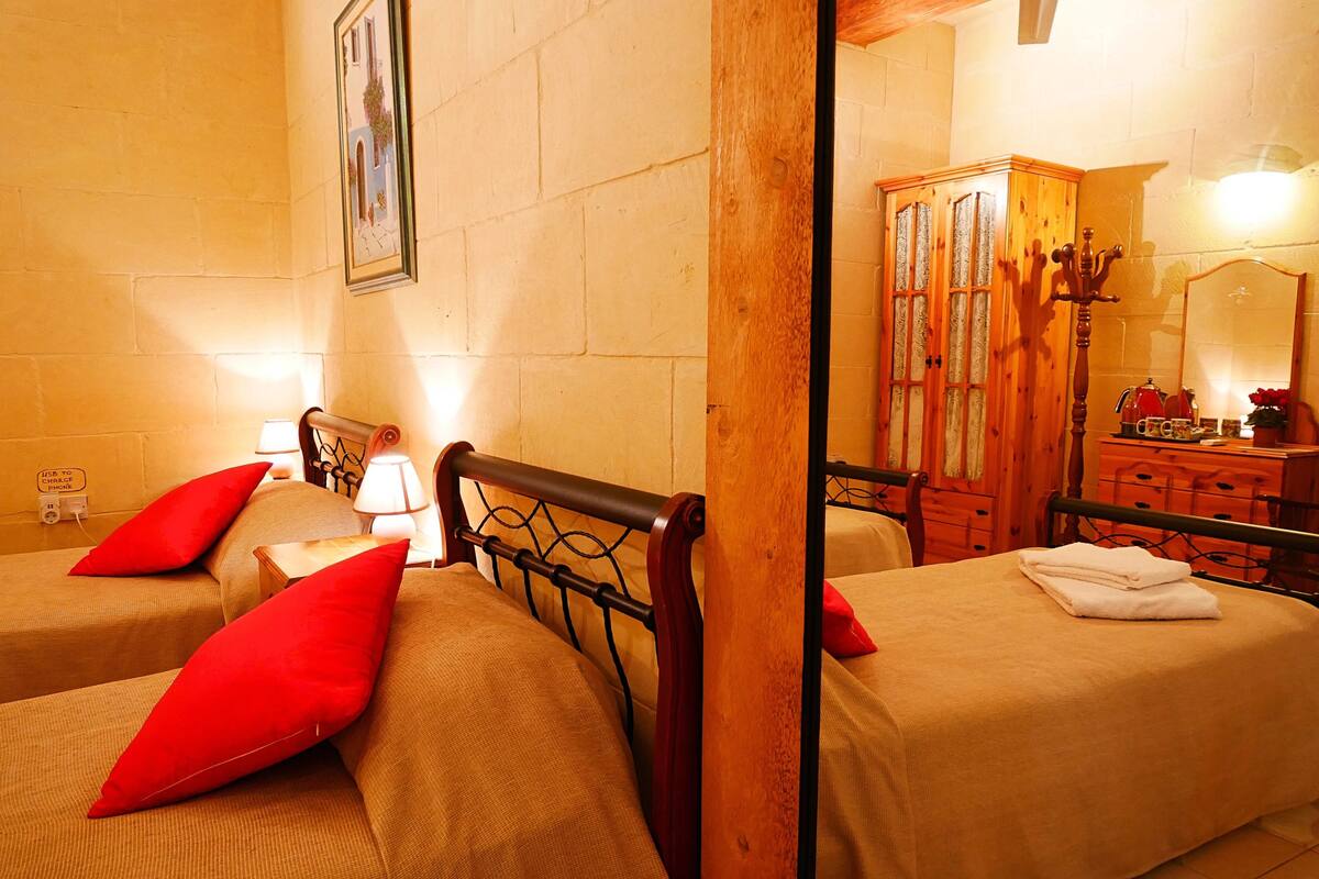 A hotel room with two beds, each with red pillows, wooden headboards, and a wooden wardrobe.