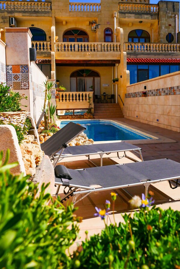 A pool area with lounge chairs and a stone building with balconies.