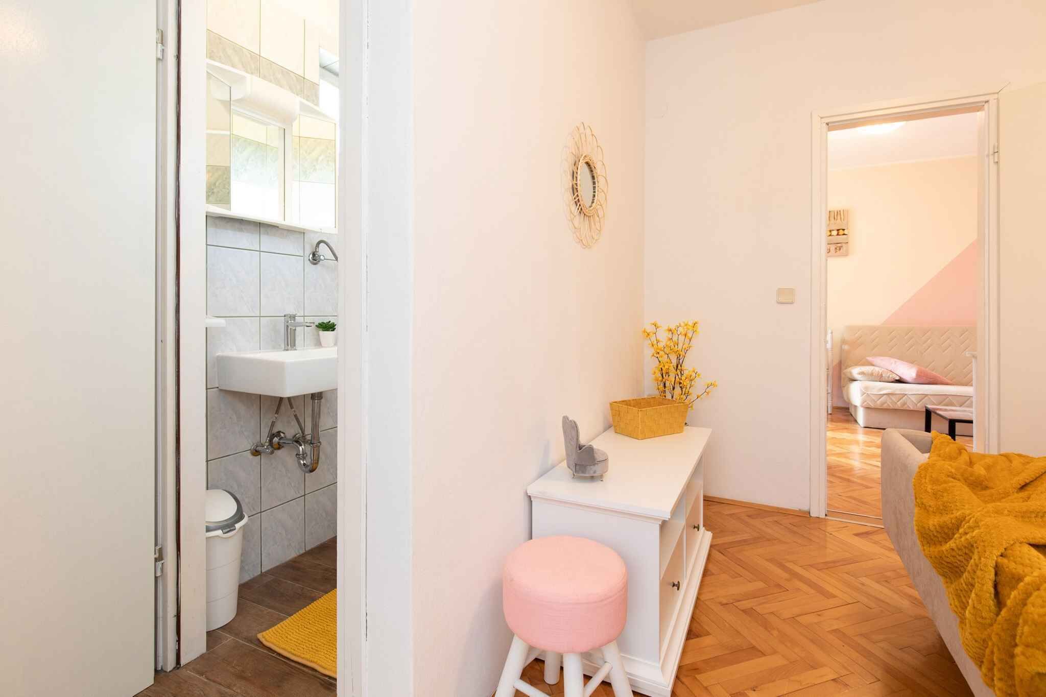 Una habitación compacta con un lavamanos blanco, un taburete pequeño, una mesita de noche con un jarrón de flores y una cama con una colcha amarilla.