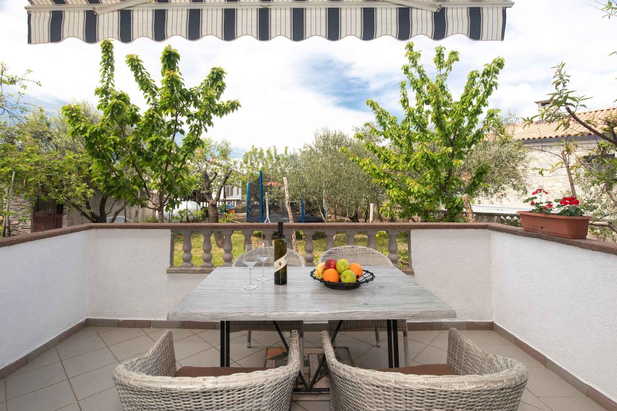 Een balkon met een tafel voor twee personen, omringd door rieten stoelen, een fles wijn en een schaal fruit.