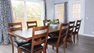 A dining area with a wooden table and chairs, large windows with curtains, and a brick wall.