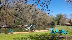A park with a playground, a pond, and Adirondack chairs.