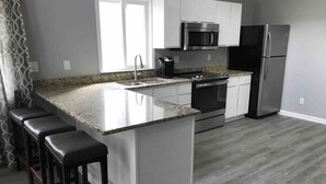 A modern kitchen with a granite countertop, white cabinetry, stainless steel appliances, and a bar stool seating area.