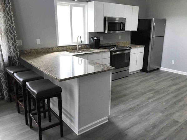 A modern kitchen with a granite countertop, white cabinetry, stainless steel appliances, and a bar stool seating area.