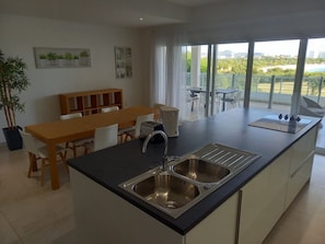 Cozinha moderna com ilha central, área de jantar e vista para uma varanda com mobiliário ao ar livre.