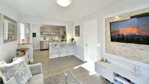 A modern living room with a large TV, a fireplace, and a kitchen in the background. - Shasta Serenity A cozy cottage in Downtown Mt Shasta (Mt Shasta)
