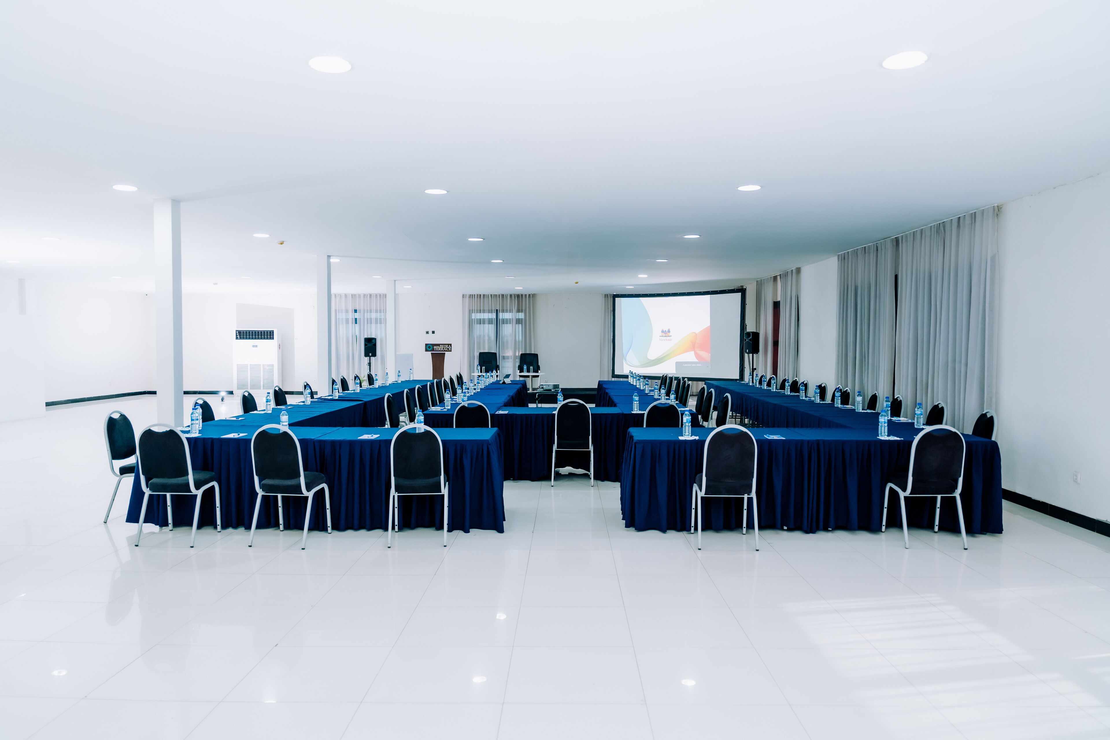 Un salón de conferencias con una larga mesa y sillas, una pantalla de proyector y una pizarra.