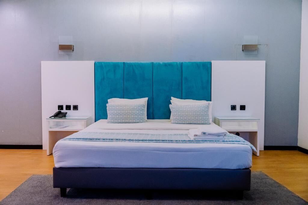 Un dormitorio moderno con una cama grande, dos mesitas de noche y un cabecero con detalles en color aguamarina.