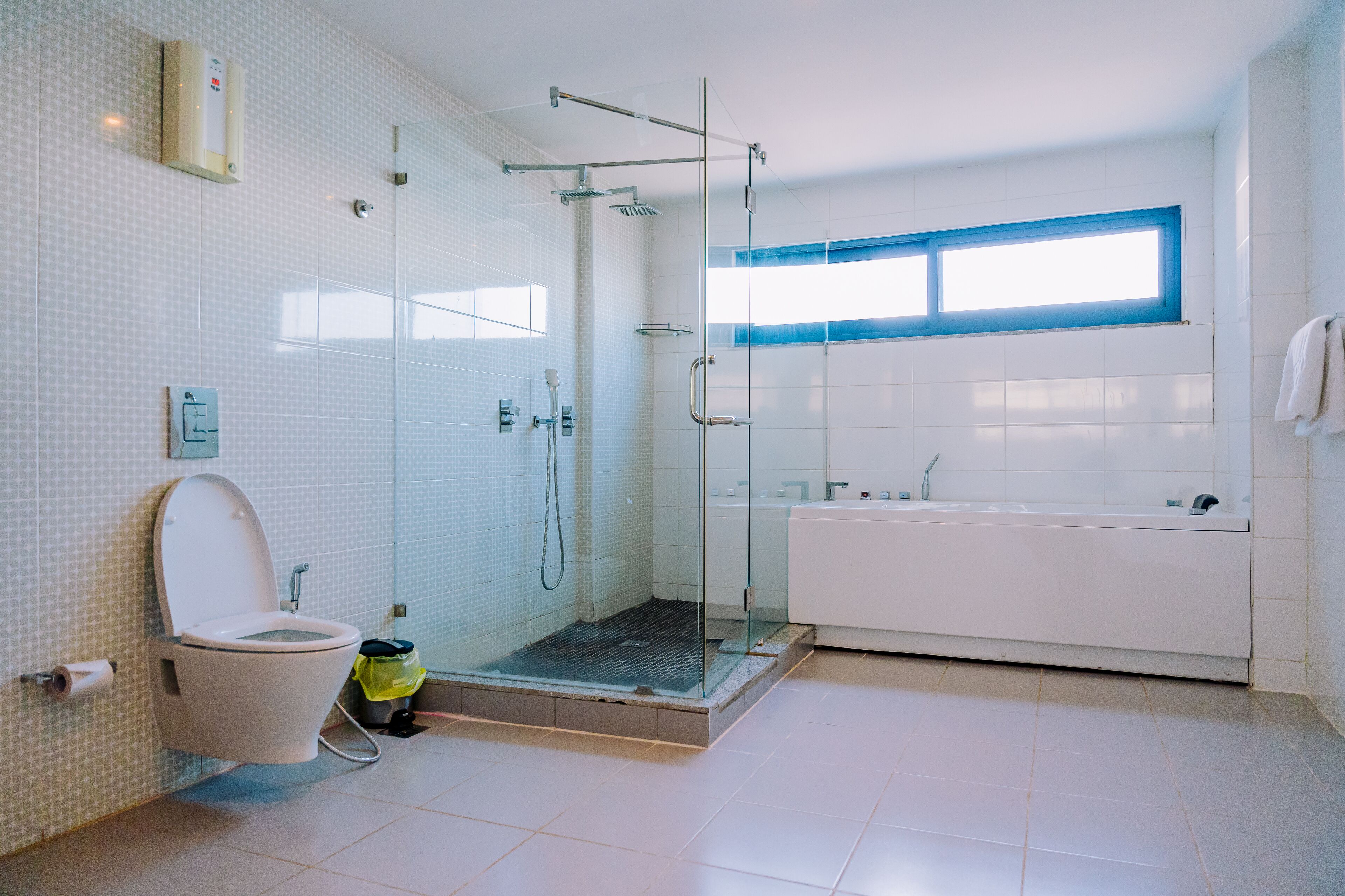 A modern bathroom with a glass-enclosed shower, a white toilet, a bathtub, and a window providing natural light.