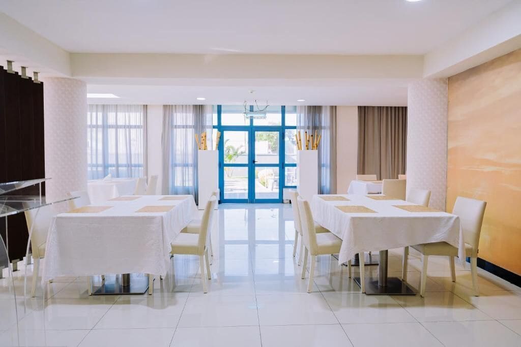 A hotel dining room with tables set for service, a clear view of the outdoors through large windows, and a modern interior design.