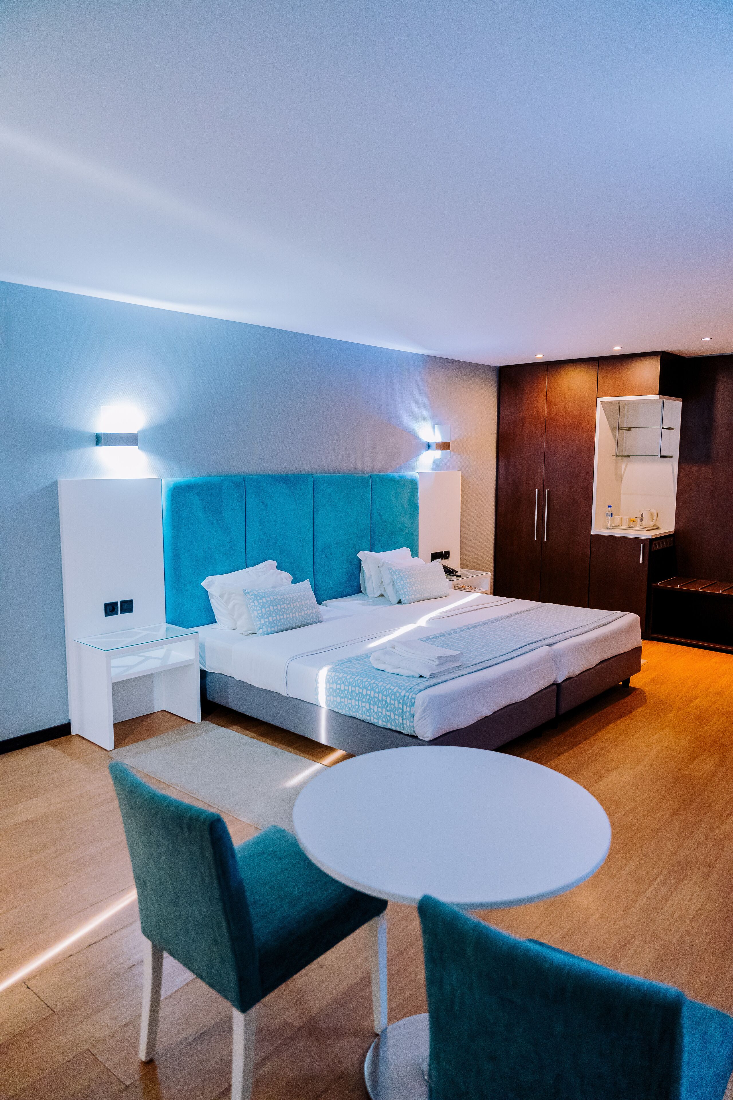 Una habitación de hotel moderna con una cama grande, una mesita de noche, una silla, una mesa redonda y un armario.