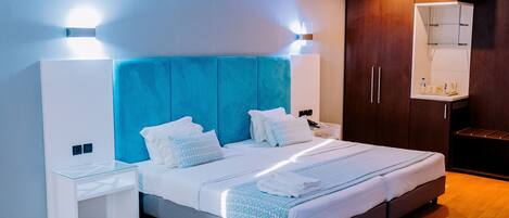 Una habitación de hotel moderna con una cama grande, una mesita de noche, una silla, una mesa redonda y un armario.