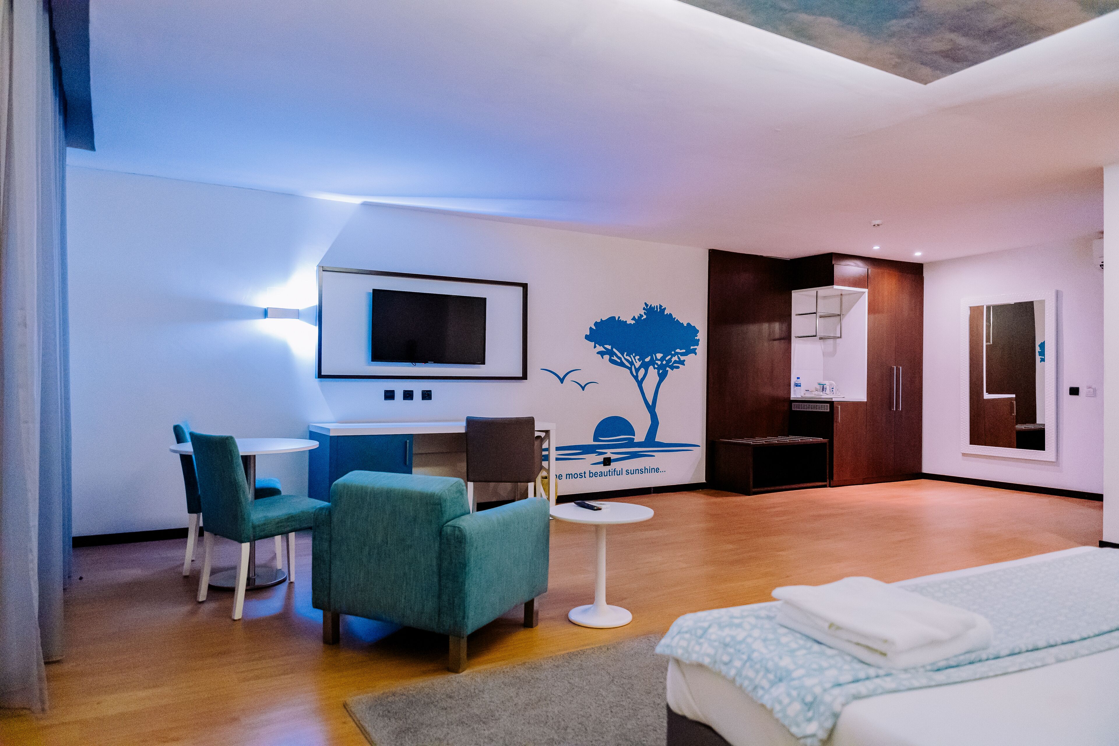 A modern hotel room with a bed, a desk with a chair, a small table, and a TV.
