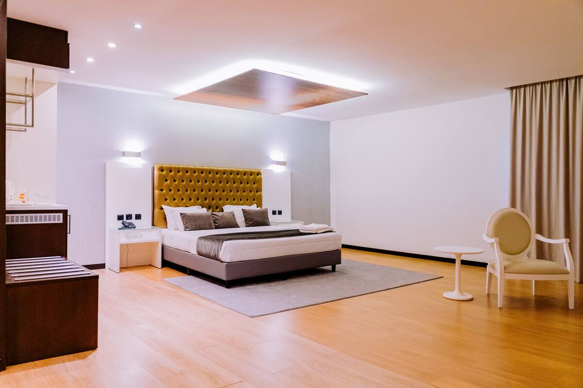 A modern hotel room with a large bed, bedside tables, a small round table, and a chair.