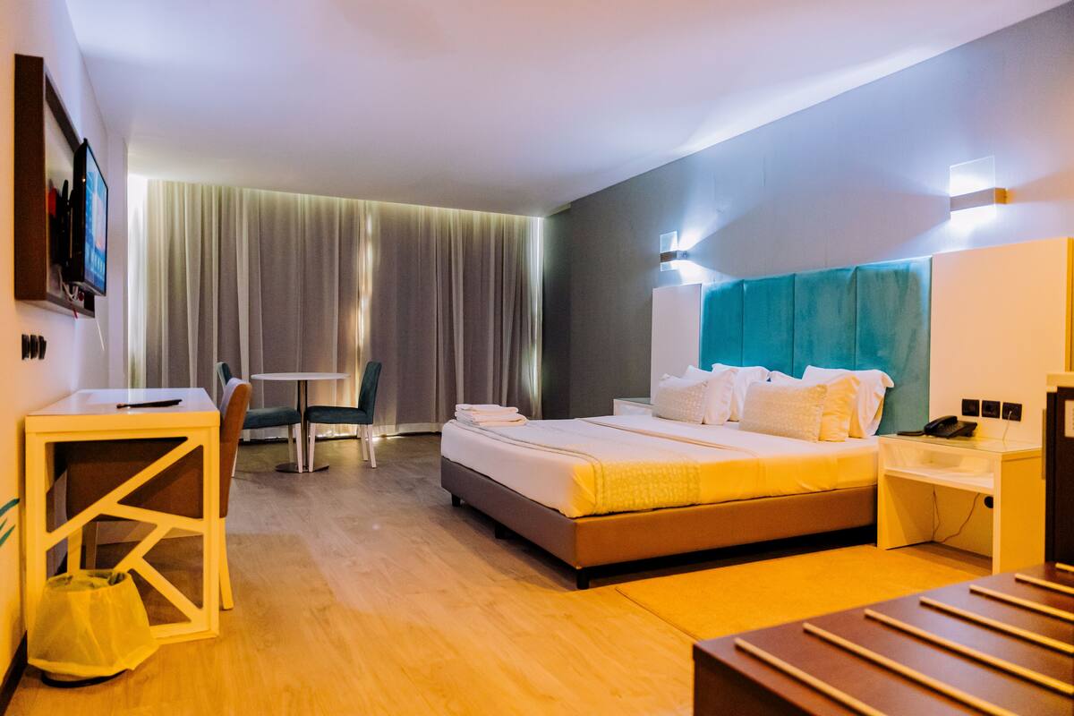 A modern hotel room with a bed, bedside table, chair, and a desk with a chair.